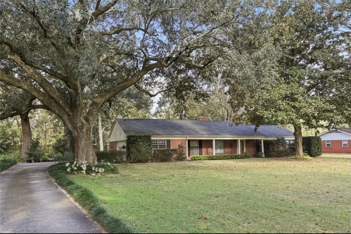Our Home, A red brick house centered between large oaks with a large front lawn and driveway down the left side.
